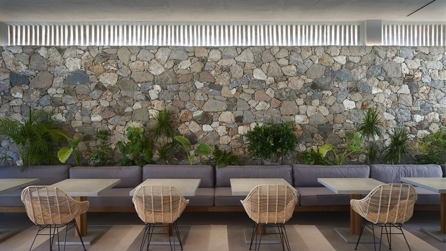 Large sofa, chairs and tables in front of a large rock wall