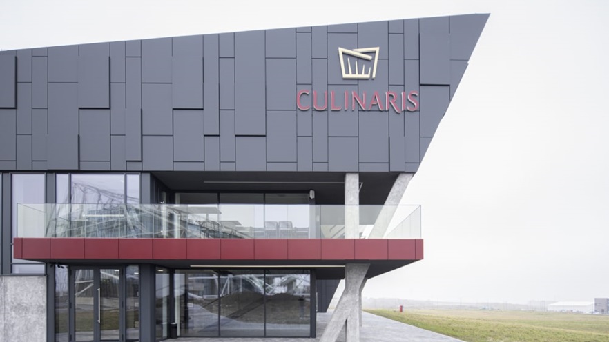 There is a balcony on top of the entrance door, there is also a large logo on the top corner of the building