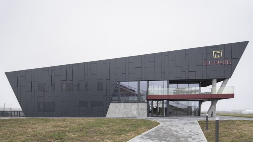 The building is covered in cladding and is surrounded by a big garden