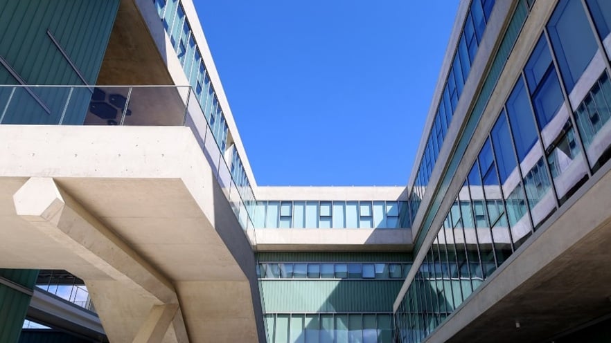 Facade of the Cyprus University of Technology building featuring a combination of solid concrete balconies with glass railings and large aluminum-framed curtain wall sections with clear glass panels