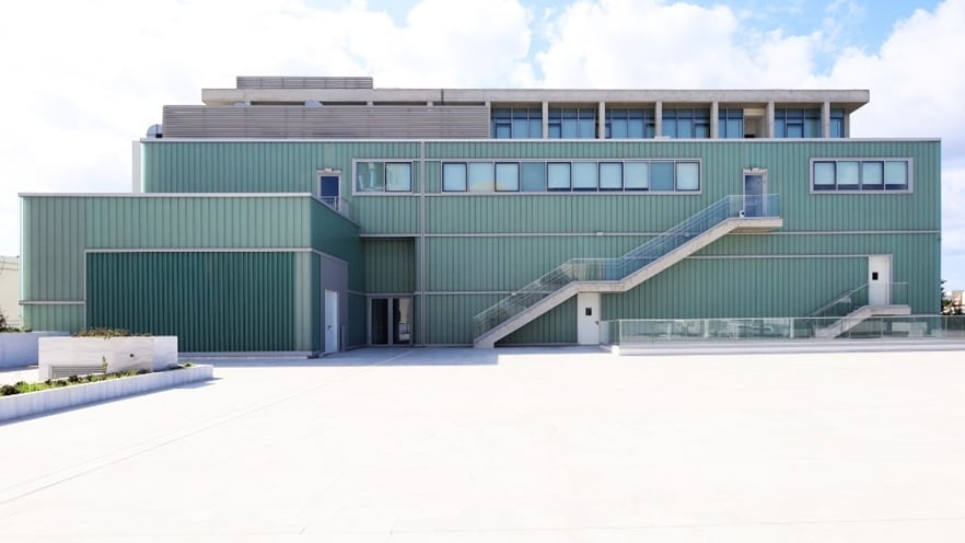 Parallelogram-shaped green building featuring aluminum elements and a staircase under a cloudy sky