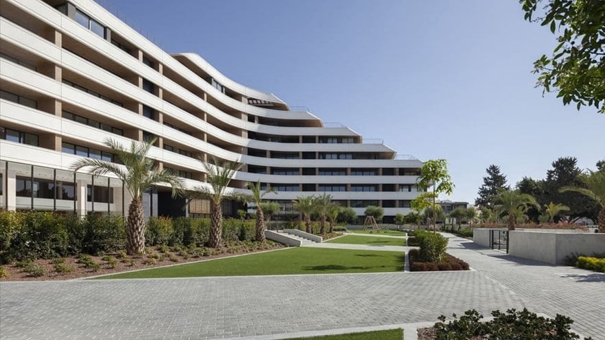 The entrance of the building is located on a large courtyard with palm trees and grass