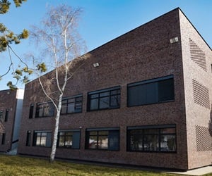 The building has brick walls and large window openings and is surrounded by a courtyard with trees and grass