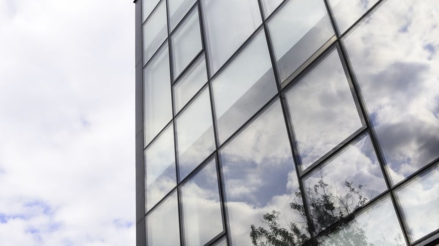The curtain wall reflects a tree and the clouds
