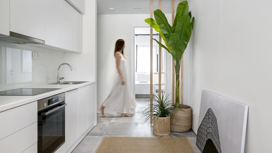 Kitchen in white tones and plants and a woman passing