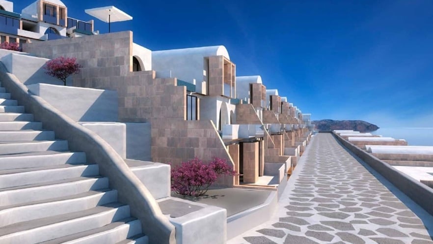 Wide paved walkway bordered by low stone walls and small plants, leading alongside white & beige buildings with balconies under a clear blue sky at Il Monte Galala