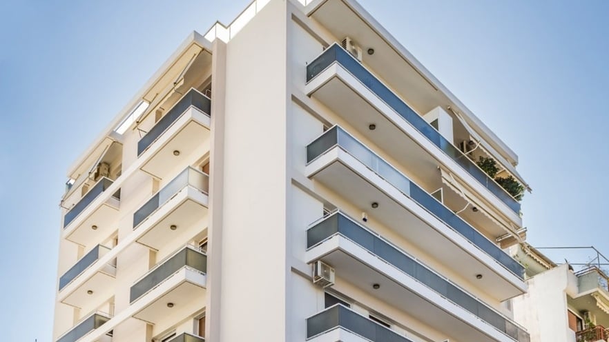 Modern multi-story apartment building with a white facade and glass balcony railings on each floor.