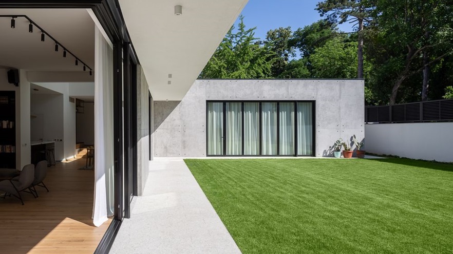 The corner sliding window is open and the indoor sitting area integrates with the garden