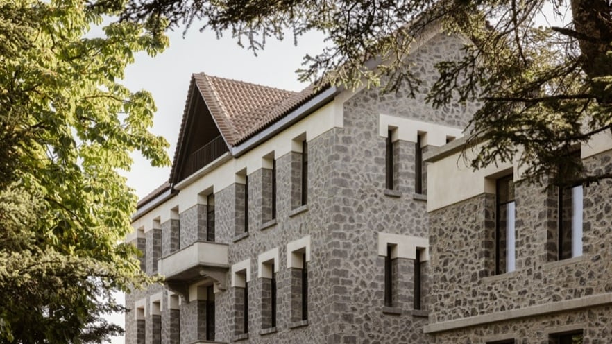 Multi-story stone building with a gabled roof and balconies, surrounded by trees.