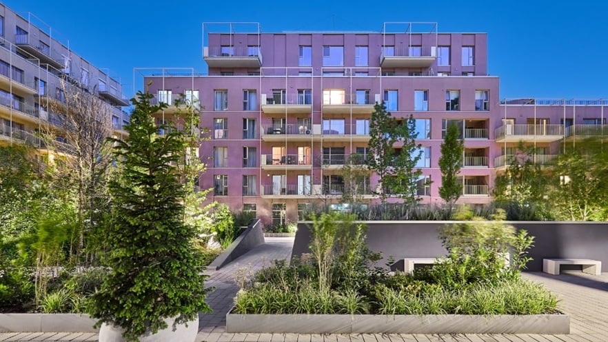 Courtyard of Marmura Residence with geometric raised plant beds, paved walkways, and a modern multi-story building featuring tan, gray, and green tones with large windows and balconies