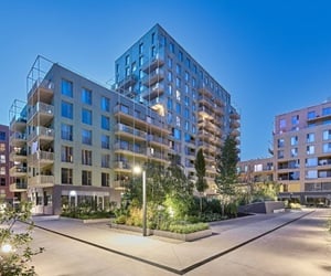 Night view of Marmura Residence courtyard with illuminated walkways, raised plant beds, and warm lighting highlighting the modern building façades and balconies