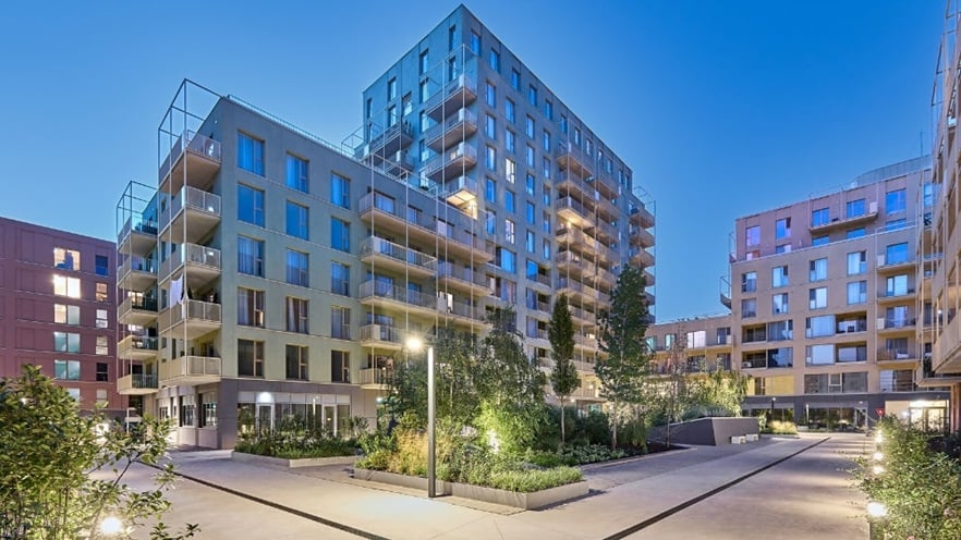 Night view of Marmura Residence courtyard with illuminated walkways, raised plant beds, and warm lighting highlighting the modern building façades and balconies