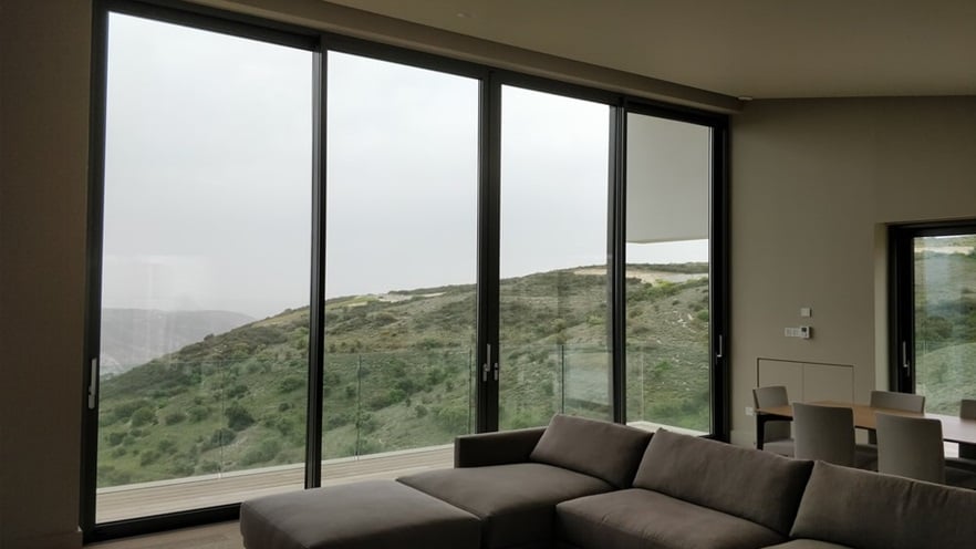 The living room has a large grey couch and a dining table in front of large windows
