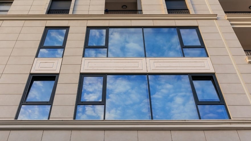 Façade of Mozart Residence with tall, narrow aluminum-framed windows in different open positions, set against a beige wall with a grid-like panel design