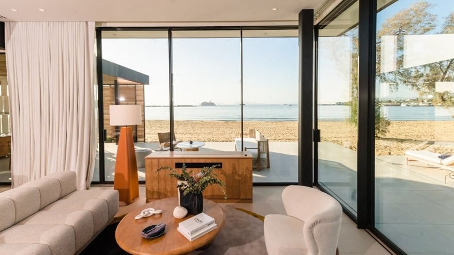 Modern living room with neutral-toned furniture and ocean view through large windows.