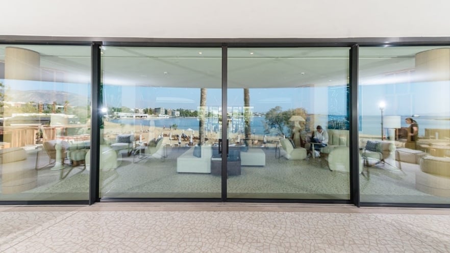 Indoor seating area with modern furniture and large glass window overlooking water, trees, and distant buildings.