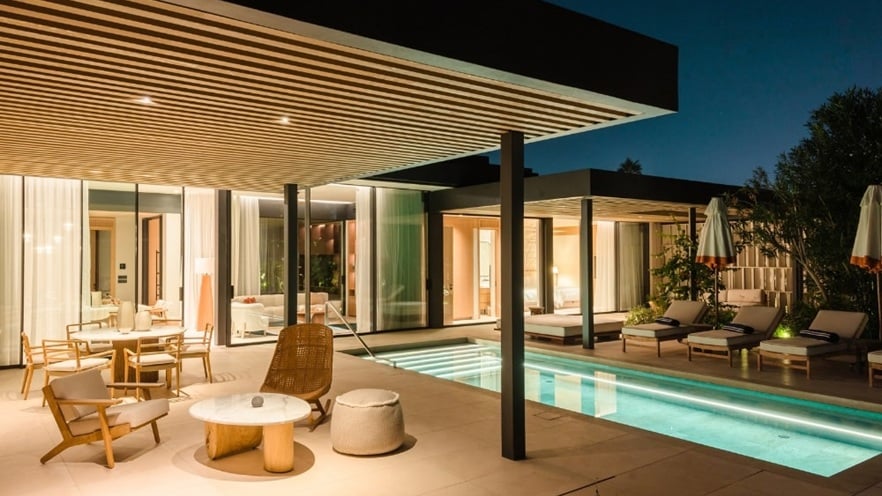 Outdoor patio at night with pool, warm lighting, and modern furniture under a wooden roof.