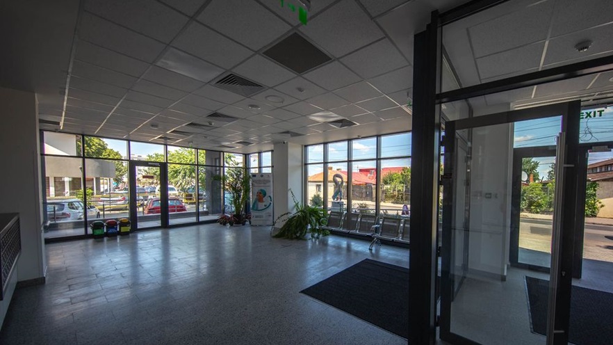 The lobby is spacious, with large glass openings and has metal chairs and plants
