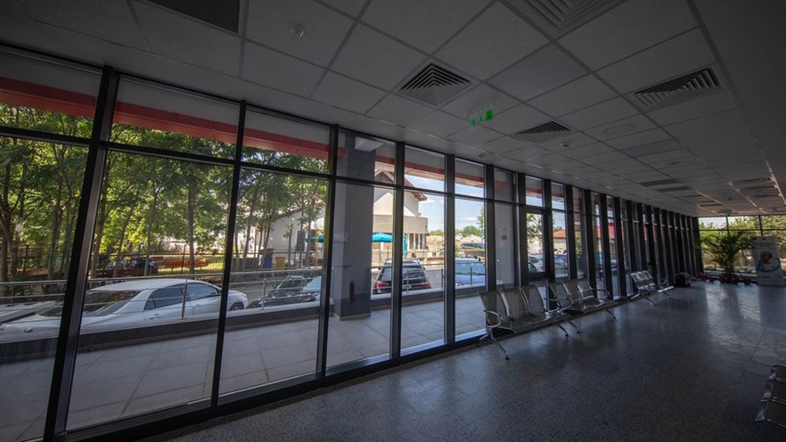 The waiting area has metal chairs and glass openings overlooking a terrace and the parking lot