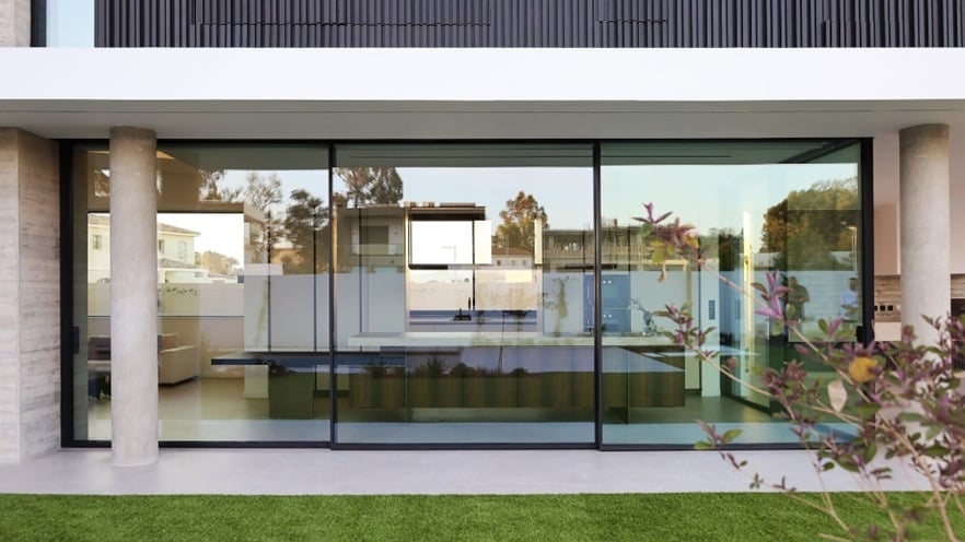 Modern building exterior with large aluminium windows, concrete pillars, and a green lawn