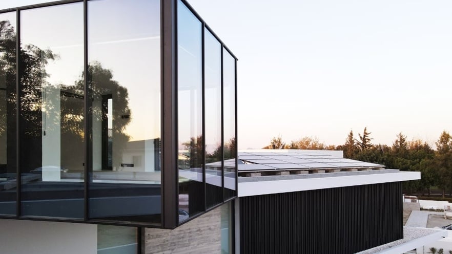 Modern architectural building with a sleek design, featuring large floor-to-ceiling glass windows, clean lines, and a mix of glass and metal materials. An overhanging section adds depth to the structure, with trees visible in the background.