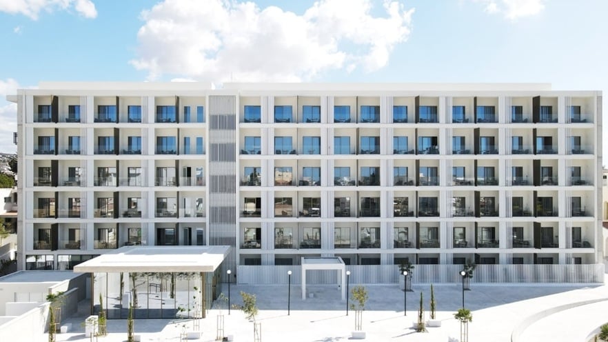 Symmetrical five-story building with white facade, vertical design elements, balconies, and an open courtyard with small trees and street lamps.