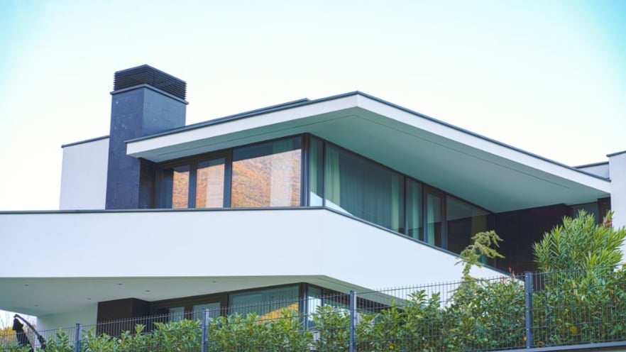 The top floor of the villa with large openings seen from the street through trees