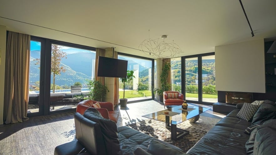 Bright living room with floor-to-ceiling aluminum windows offering a view of the pool and garden