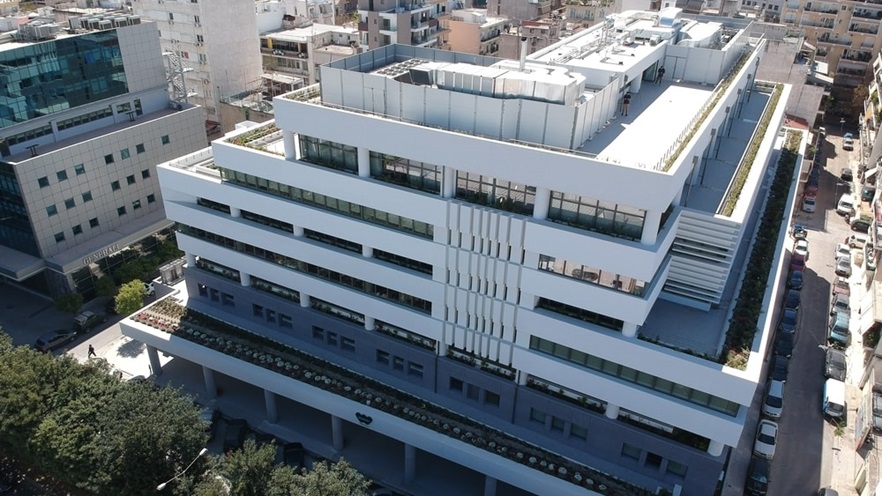 The multi-storey building is white and grey, and has plants on the balconies