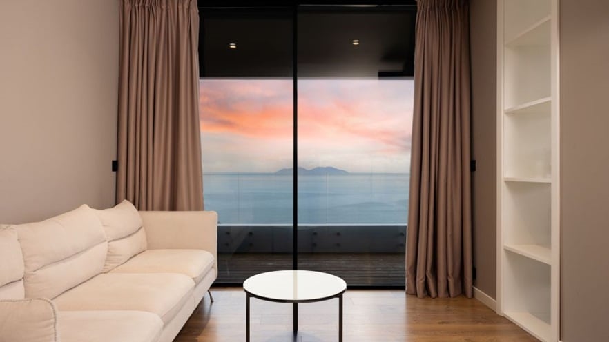 A minimal living room with white furniture, overlooking the sea at dawn through a sliding window