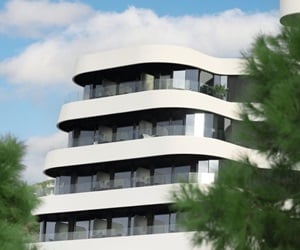 Modern building with white, curved balconies seen in between trees.
