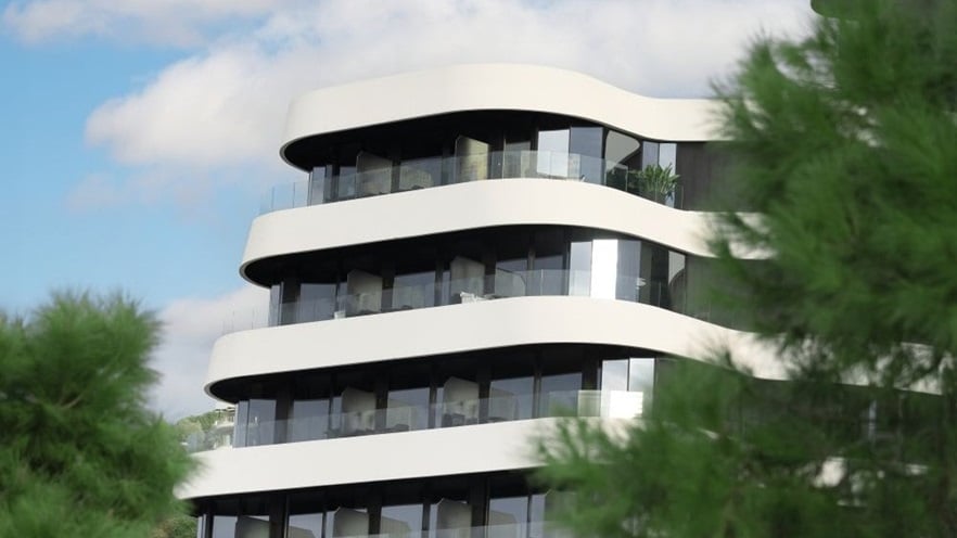 Modern building with white, curved balconies seen in between trees.